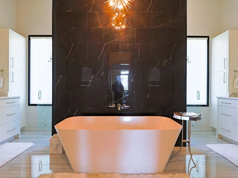Bathroom with freestanding bathtub, double vanities, black stone feature wall, and lighting