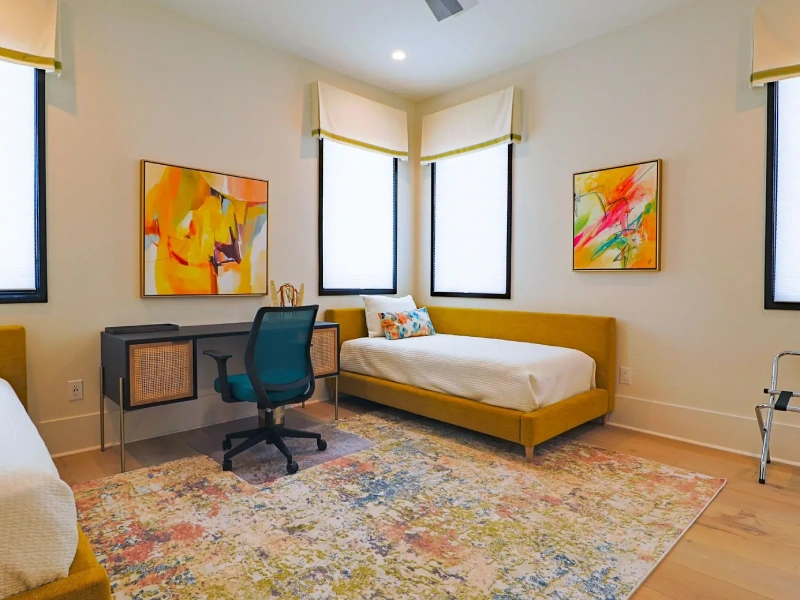 Bedroom interior with colorful rug, twin beds, study desk, and large windows