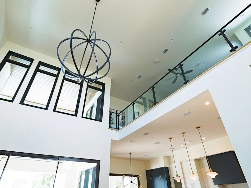 High-ceiling living space with tall windows, staircase, and statement pendant light