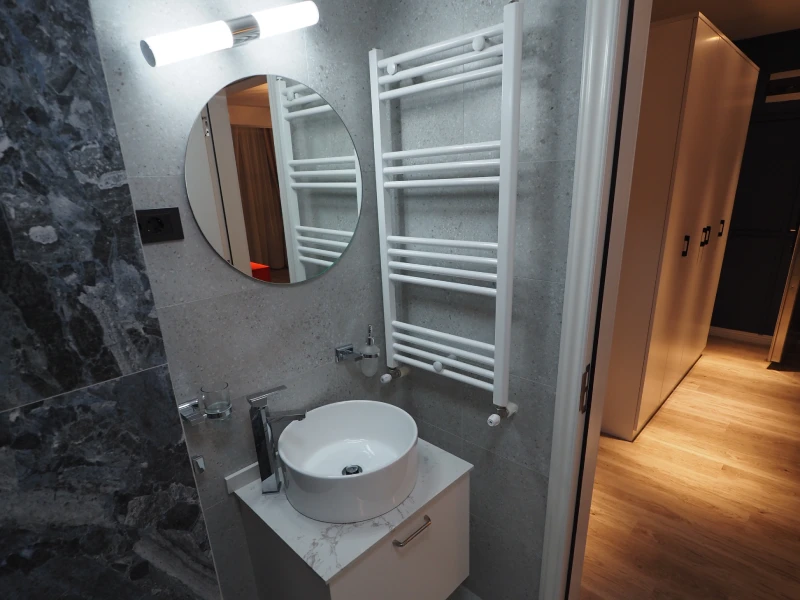 Apartment bathroom with vanity, toilet, mirror, and grey wall tile finish