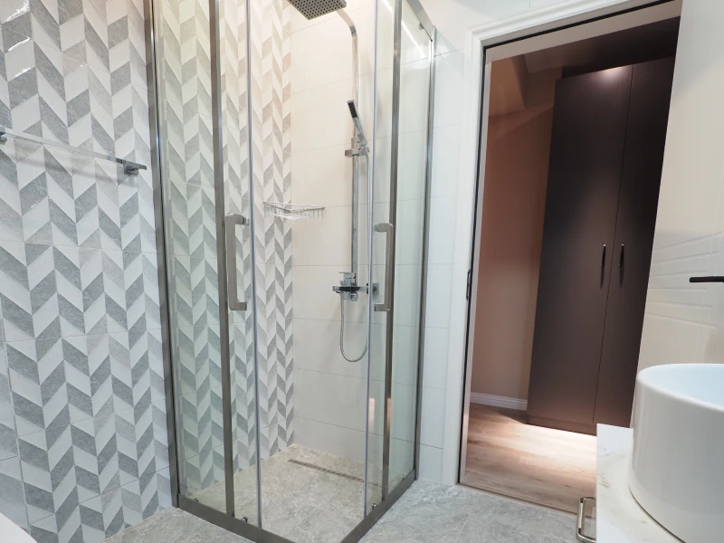 Apartment bathroom glass shower area with grey tile walls and shower fittings